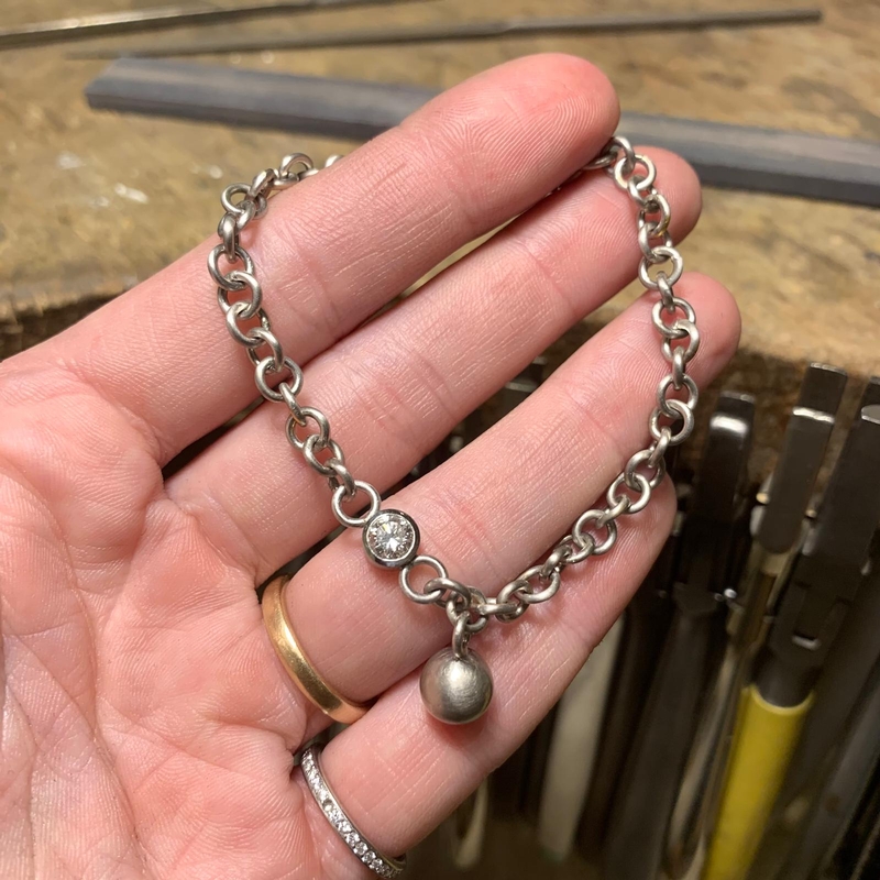 Auf einer Handfläche liegt ein PlatinArmband aus großen Ösen mit einer Kugel als Anhänger und einem Brillant in einer schlichten Fassung
