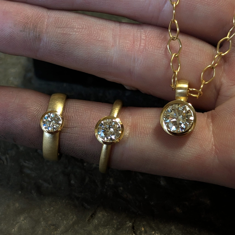 Zwei goldene Ringe und ein Anhänger mit Brillanten in unterschiedlichen Größen liegen auf einer Hand