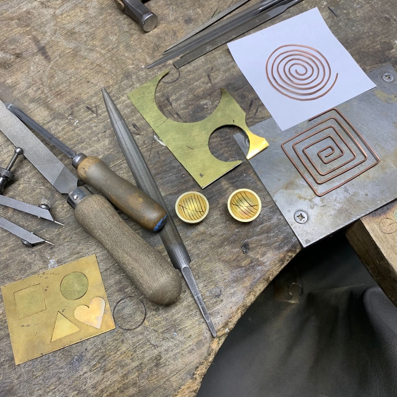 verschiedenes Werkzeug und Arbeitsproben in Messing liegen auf einem Holztisch