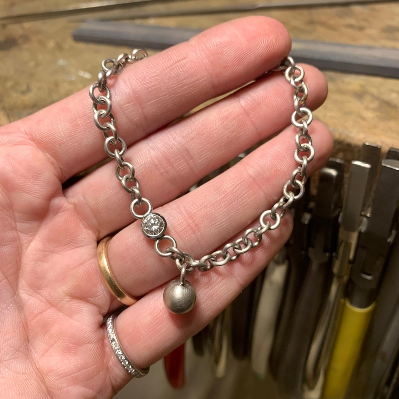 Ein Armband aus kräftigen Platinösen mit Brillant und eingehängter Kugel liegt in einer Handfläche