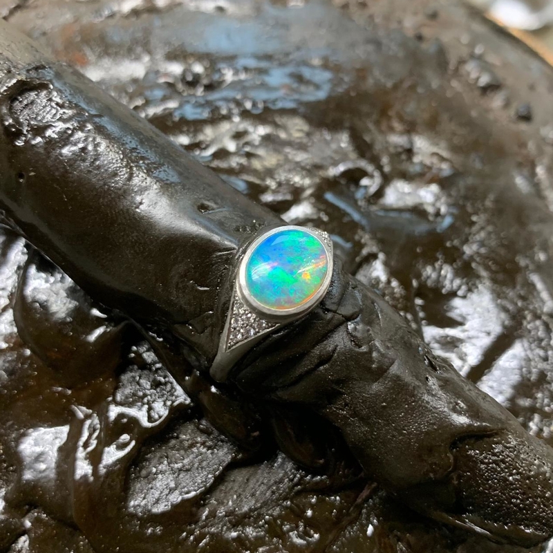 ein Platinring mit ovalem Opal, auf den Ringschultern eingefasst von 6 dreieckig angeordneten Brillanten in schwarzem Kitt