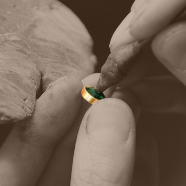 Ein grüner Edelstein wird vorsichtig in die goldene Fassung eingesetzt.