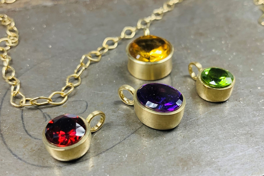 Kleine Kettenanhänger aus Gold mit Edelsteinen in kräftigen Farben.